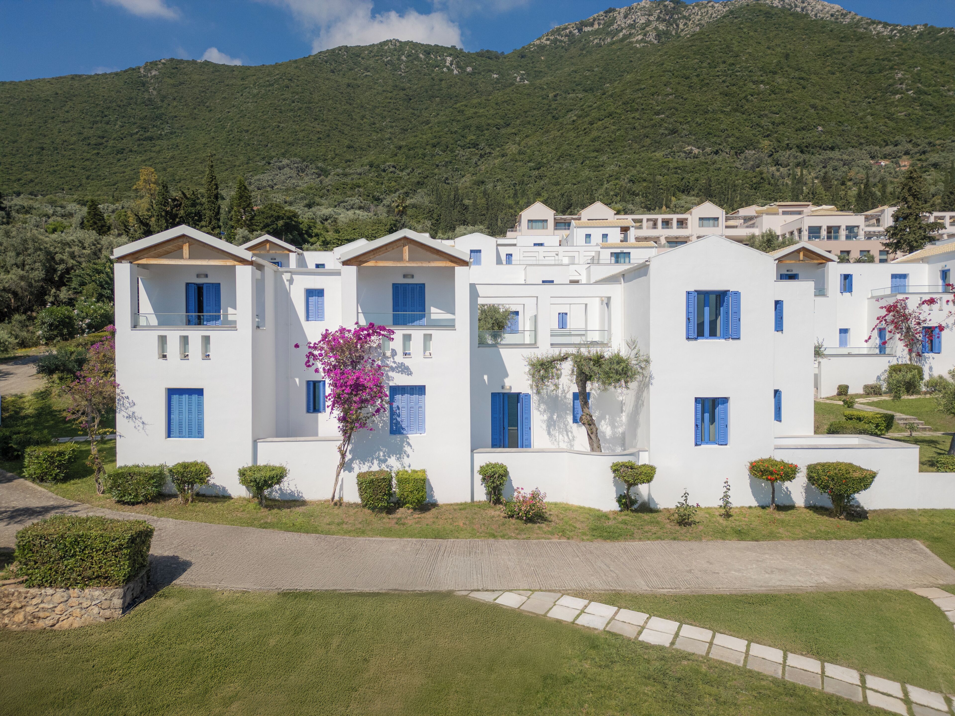 A row of white buildings with blue shutters, a paved walkway, and a mountain in the background.