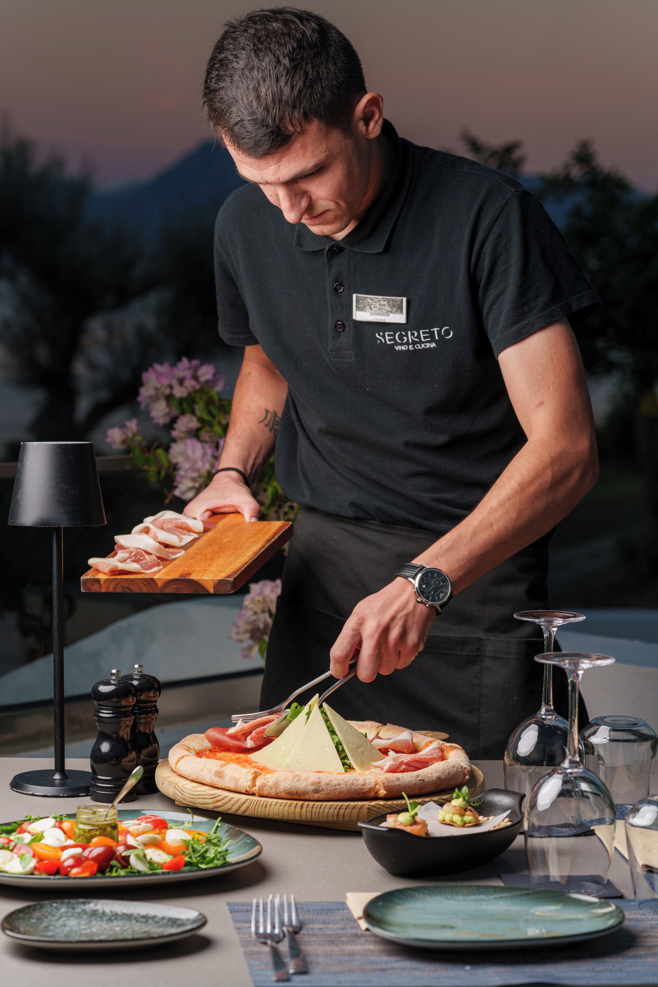 Une personne servant des plats à une table, notamment une pizza, une salade et d’autres mets.
