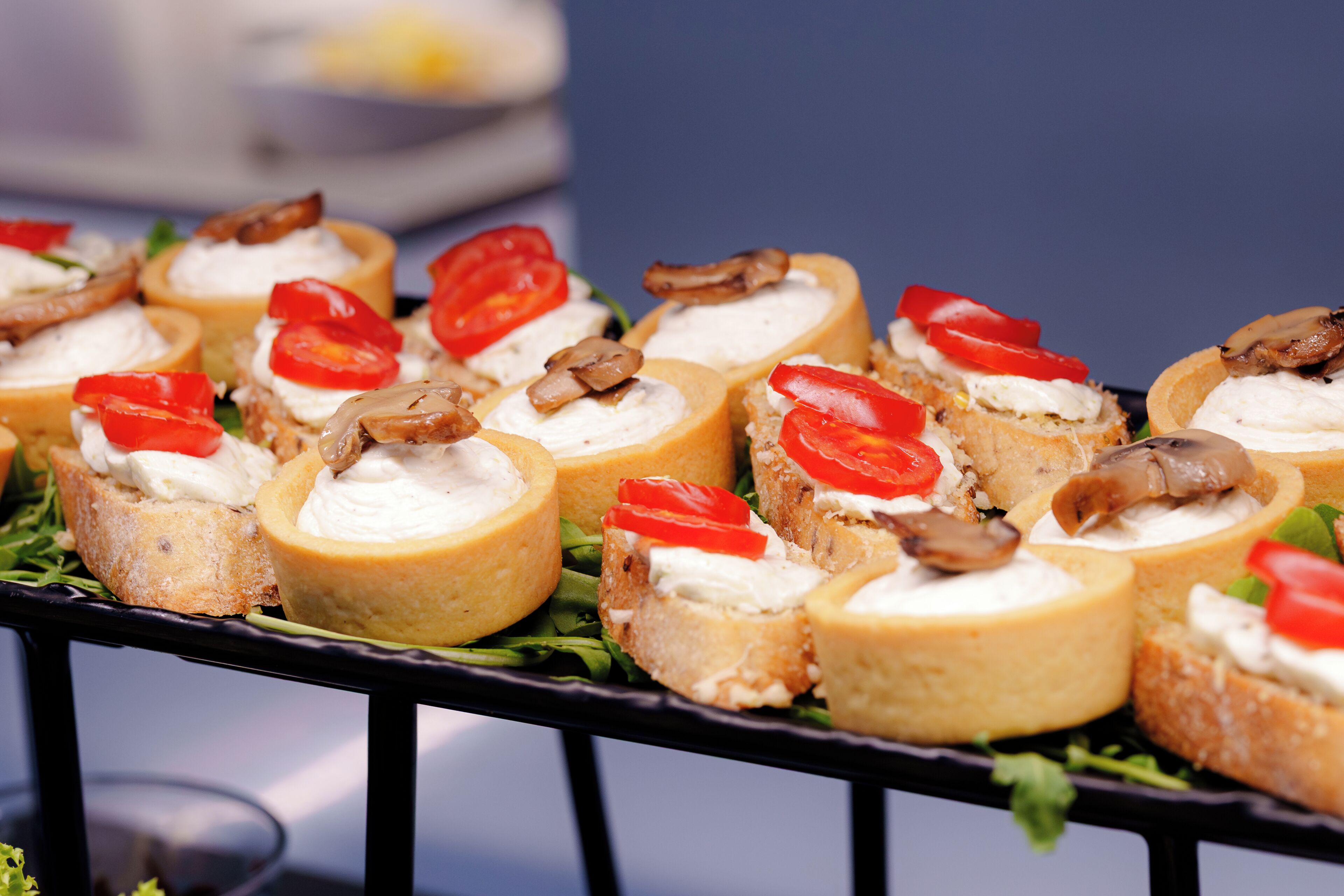 A tray of appetizers with bread rolls, cream cheese, tomatoes, and mushrooms.
