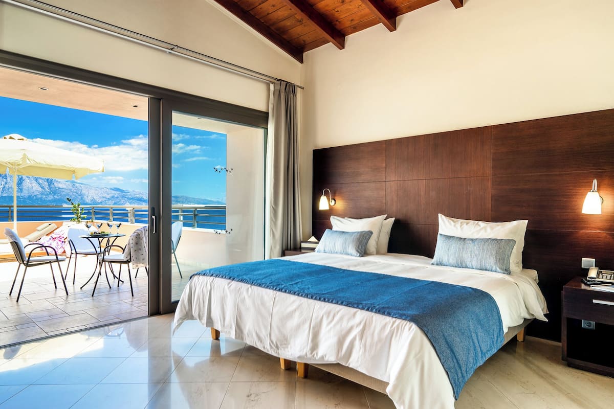 A bedroom with a large bed, a wooden headboard, two bedside lamps, and a view of a balcony with outdoor furniture.