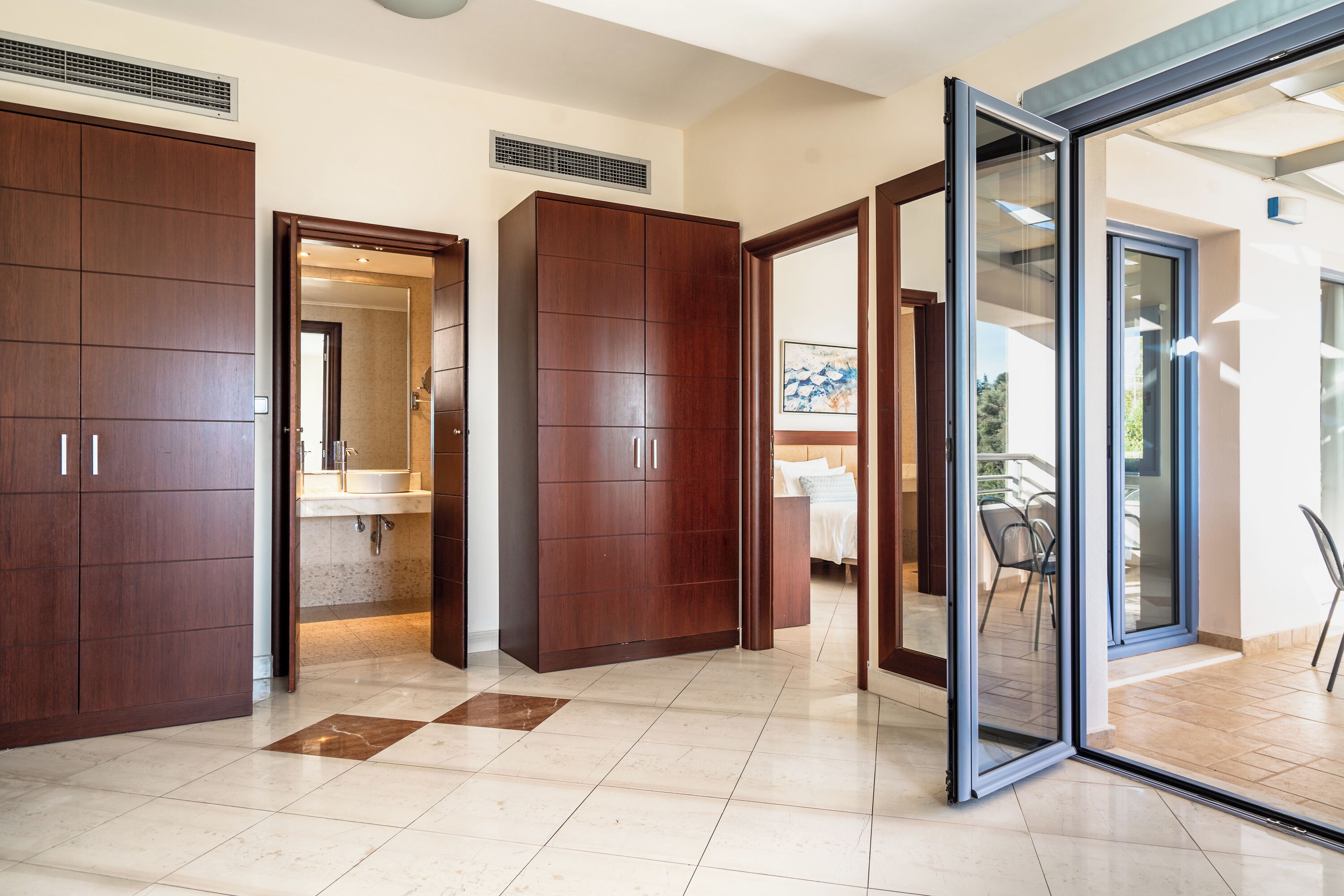 Una habitació d'hotel moderna amb un armari ampli, un bany amb rentaplat i mirall, i una porta corredissa de vidre que dona a una zona exterior.