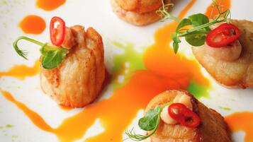 A white plate with four food items, each topped with a red chili slice and a green leaf, surrounded by orange sauce.