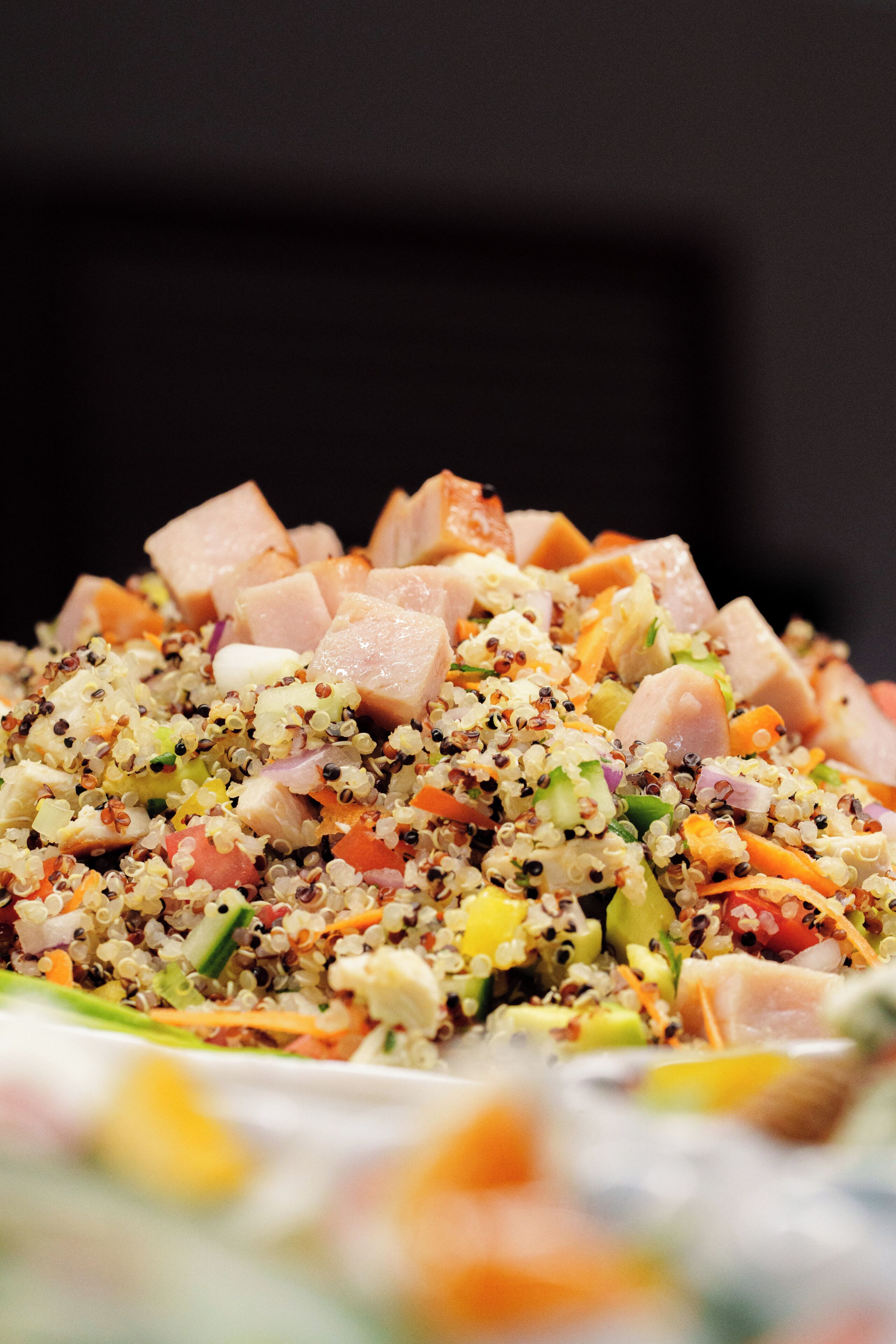 A close-up of a quinoa salad with various vegetables and diced meat.