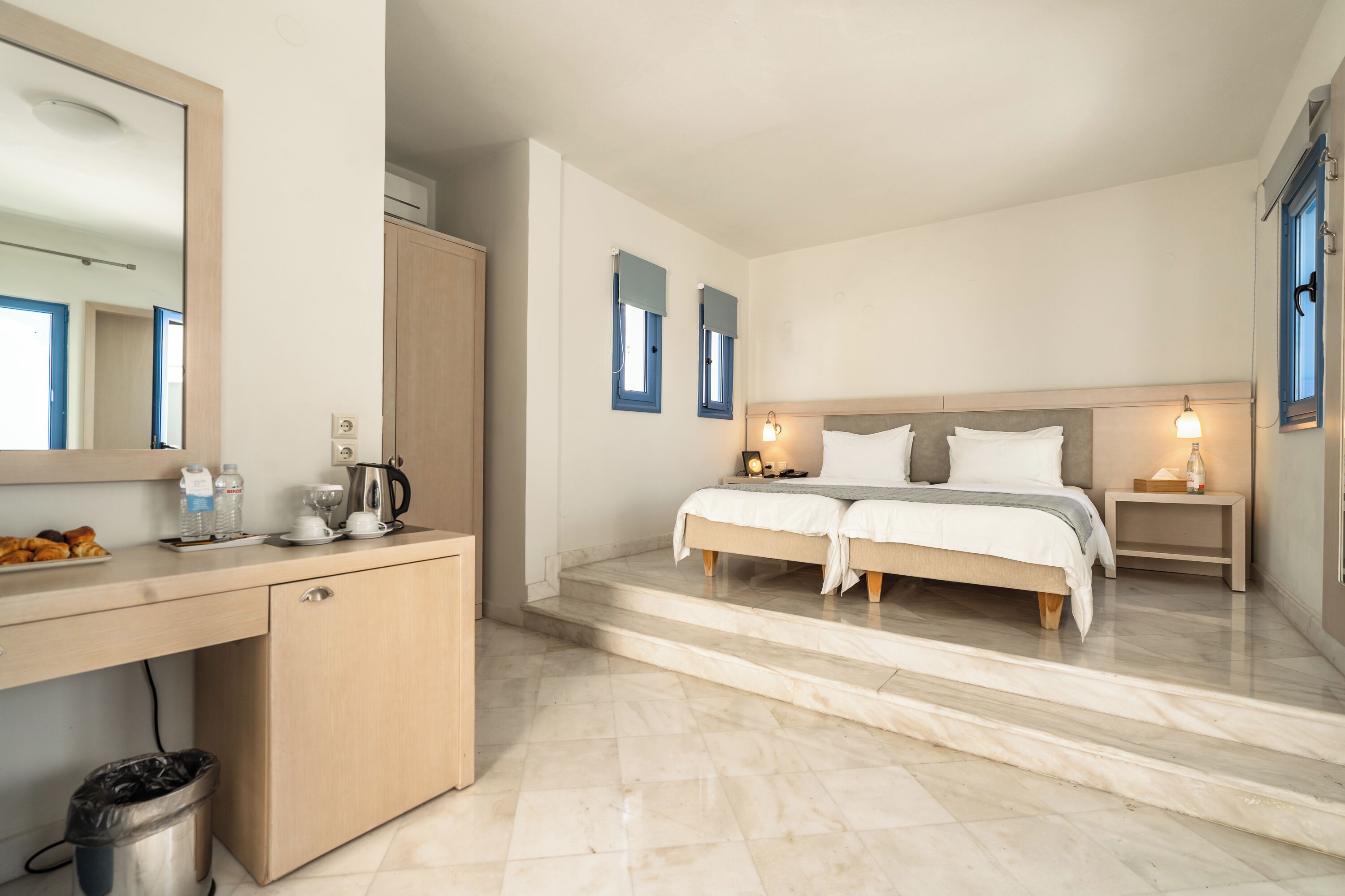 A bedroom with a bed, bedside tables, a desk, and a trash bin.