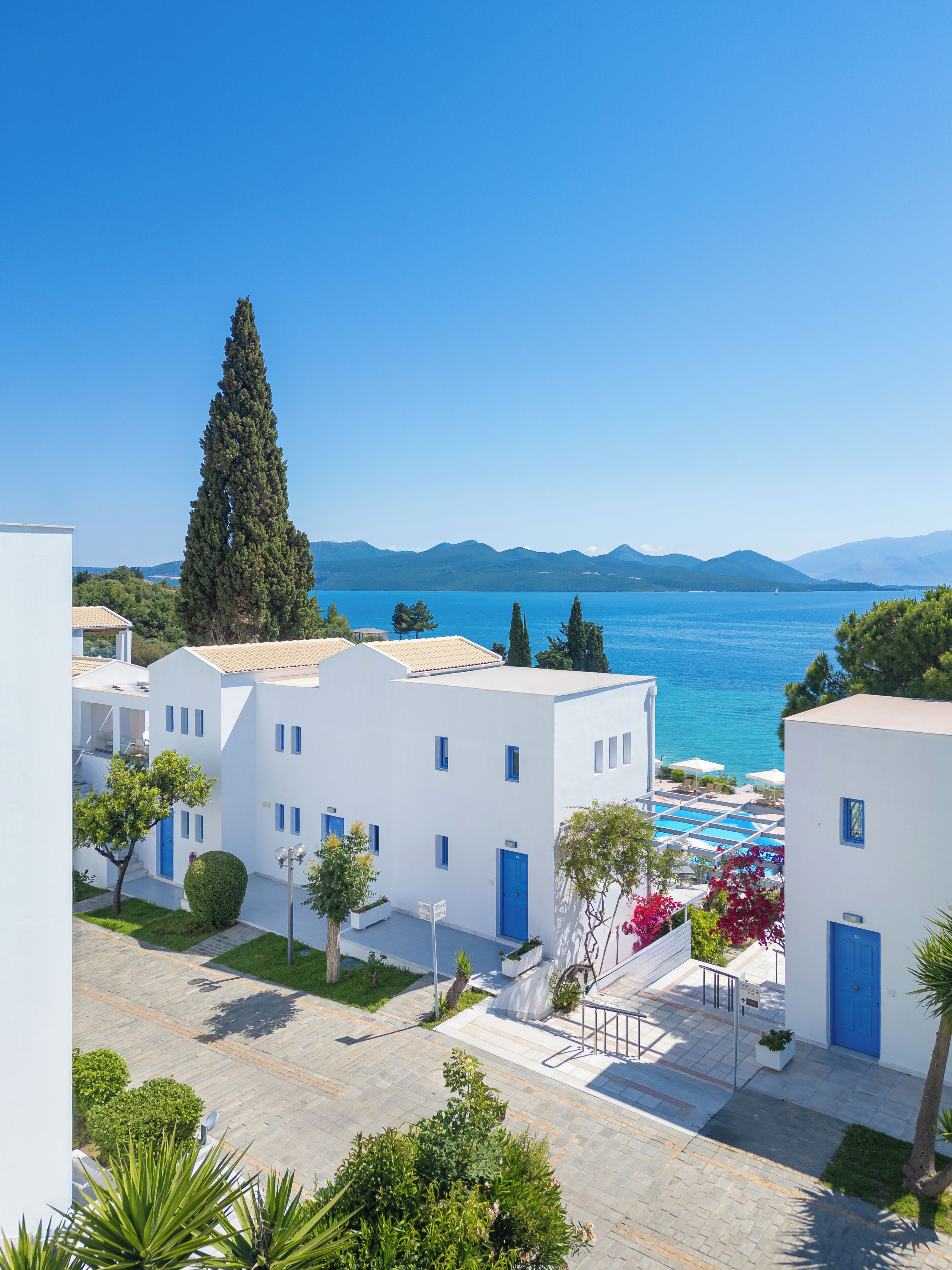 Un hotel frente al mar con edificios blancos, puertas azules y zona de piscina.