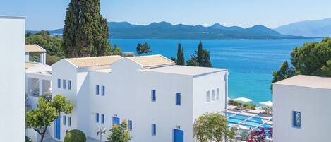 Un hotel frente al mar con edificios blancos, puertas azules y zona de piscina.