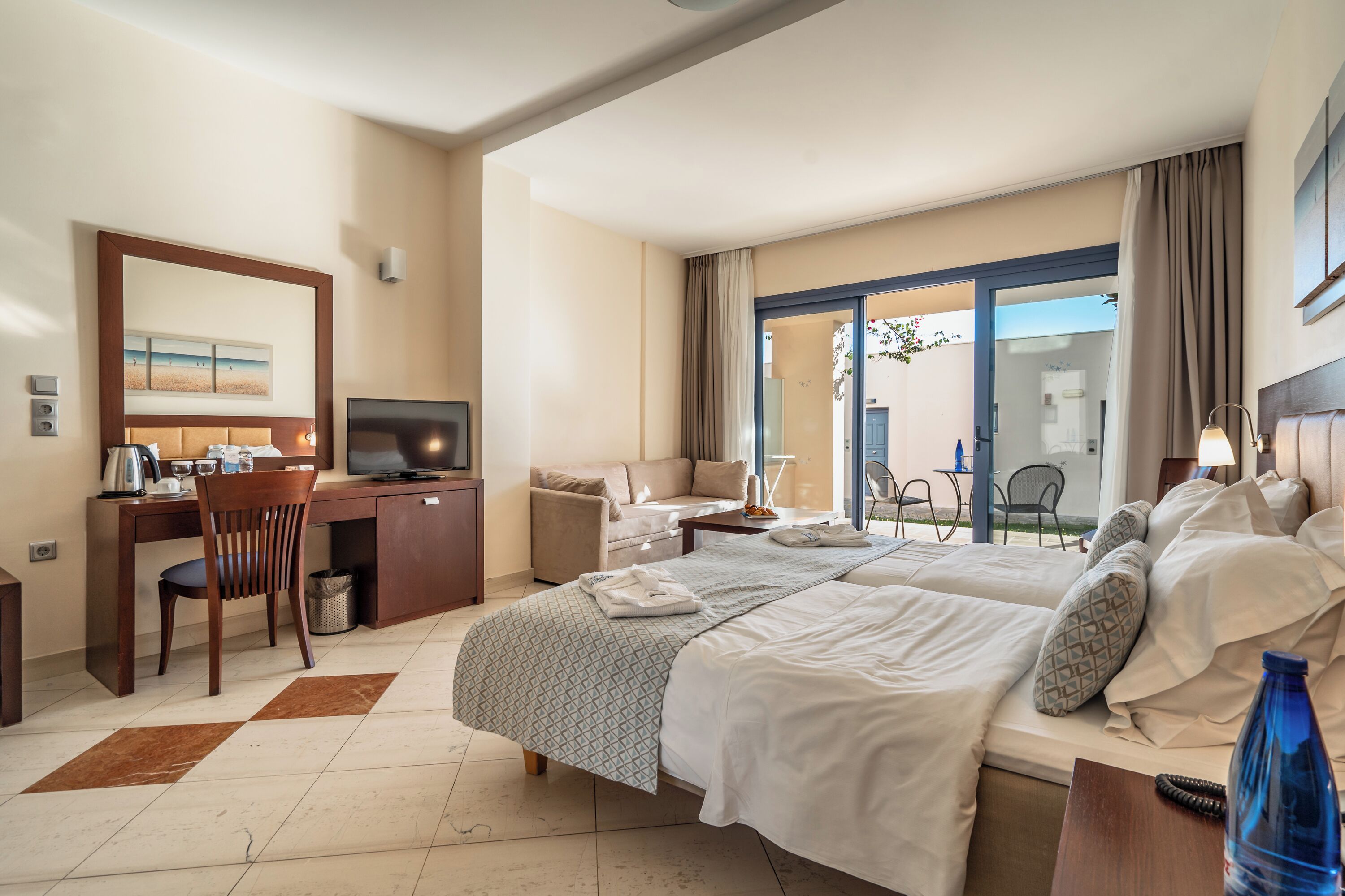 A hotel room with a bed, desk, chair, TV, and a view of the outdoors.