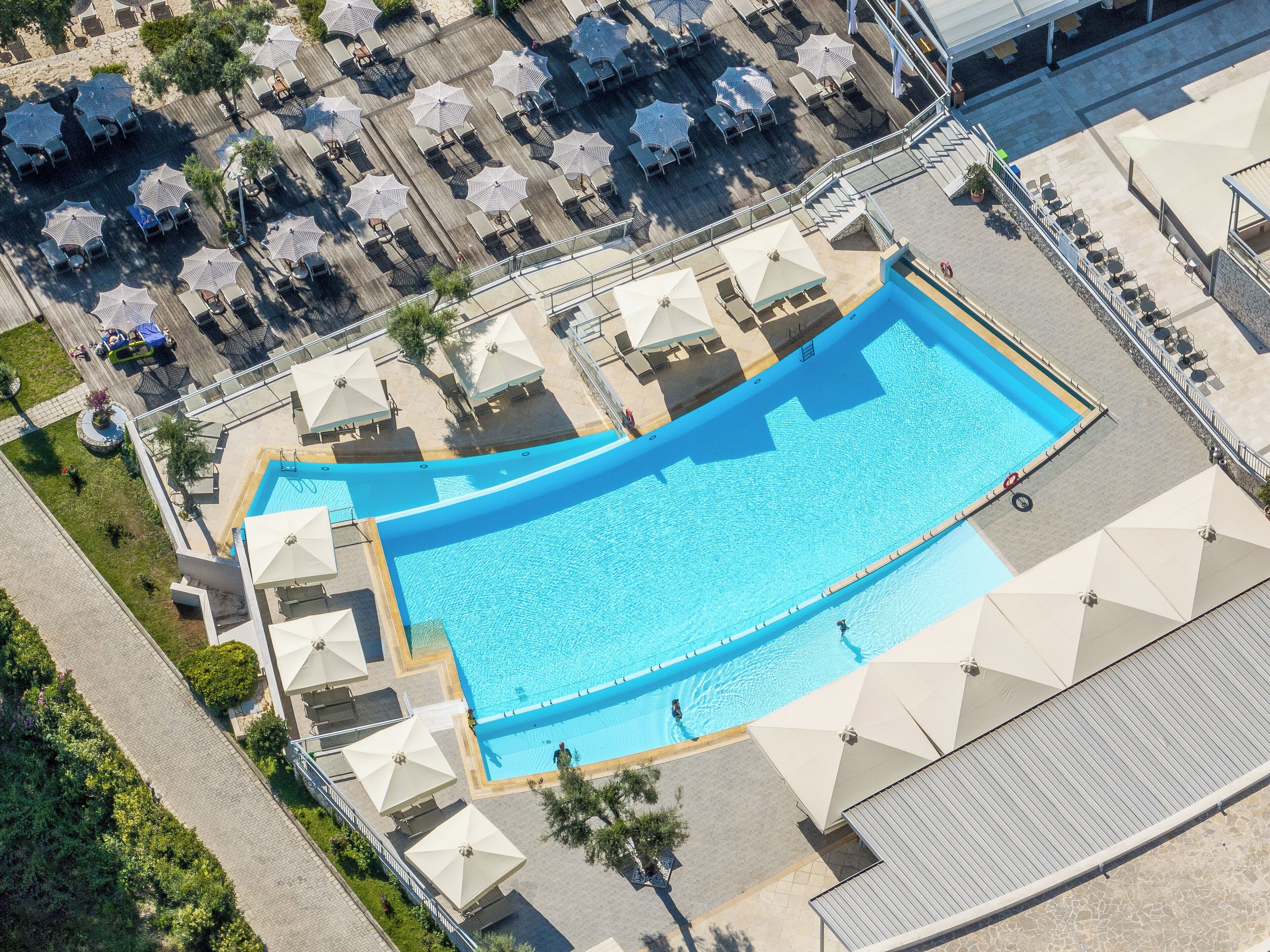 An aerial view of a swimming pool area with multiple sun loungers and umbrellas.