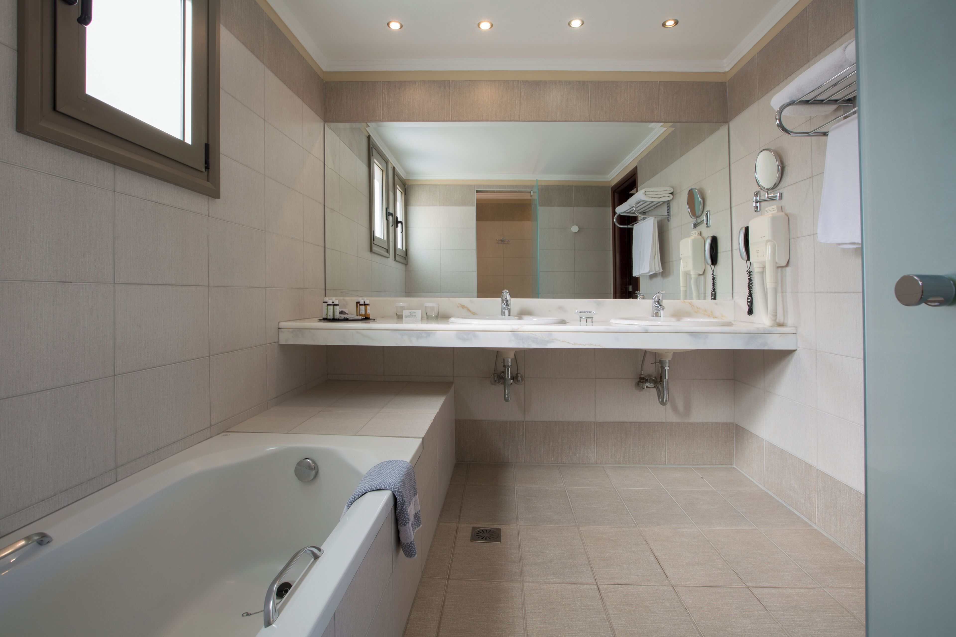 A modern bathroom with a bathtub, two sinks, a large mirror, and a shower.