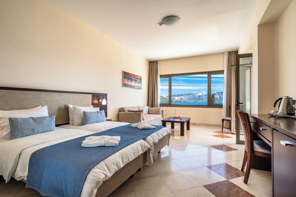 A hotel room with a large bed, a desk, a chair, a small table, and a view of the mountains through the window.