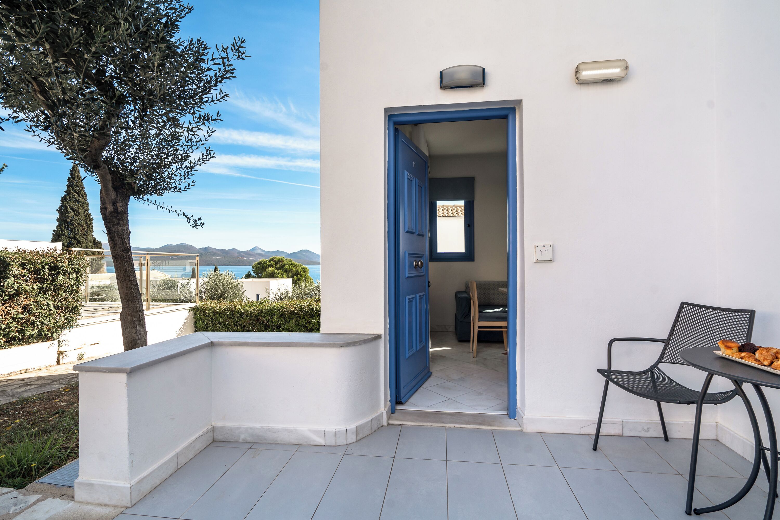 A balcony with a white wall, a blue door, and a table with a chair.