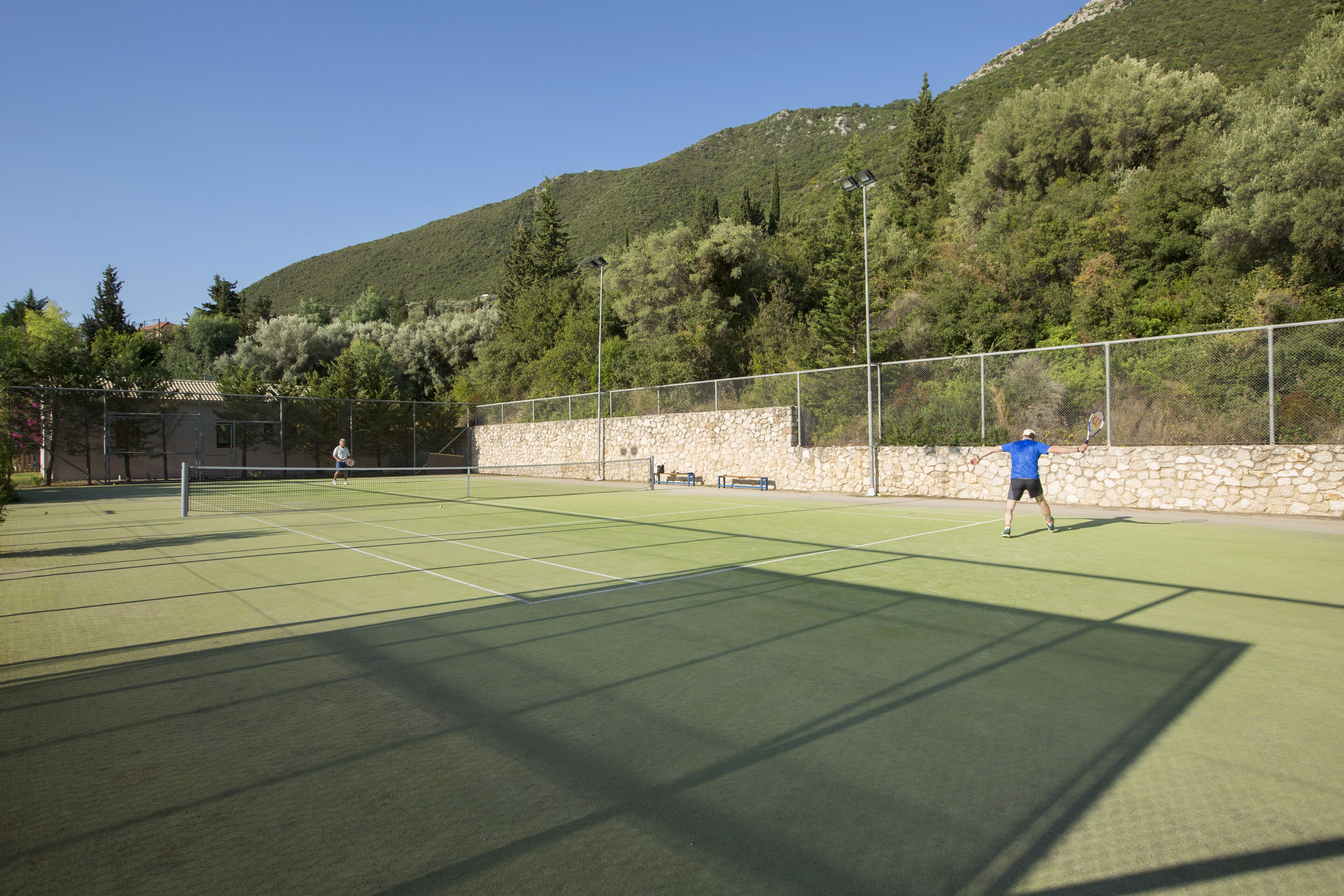 An outdoor tennis court with a stone wall and trees in the background.