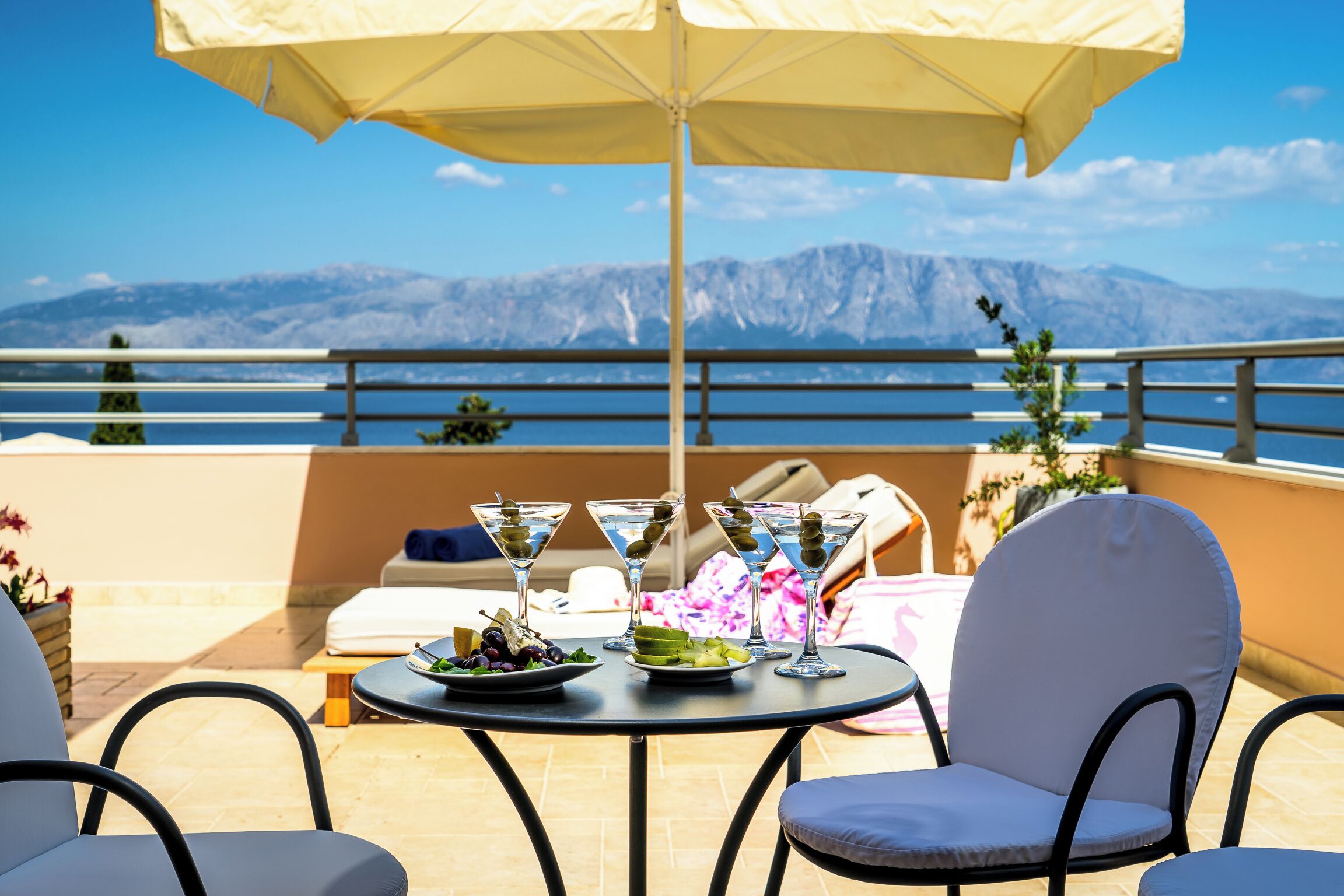 A terrace with a table set for drinks, a view of mountains, and a pool.