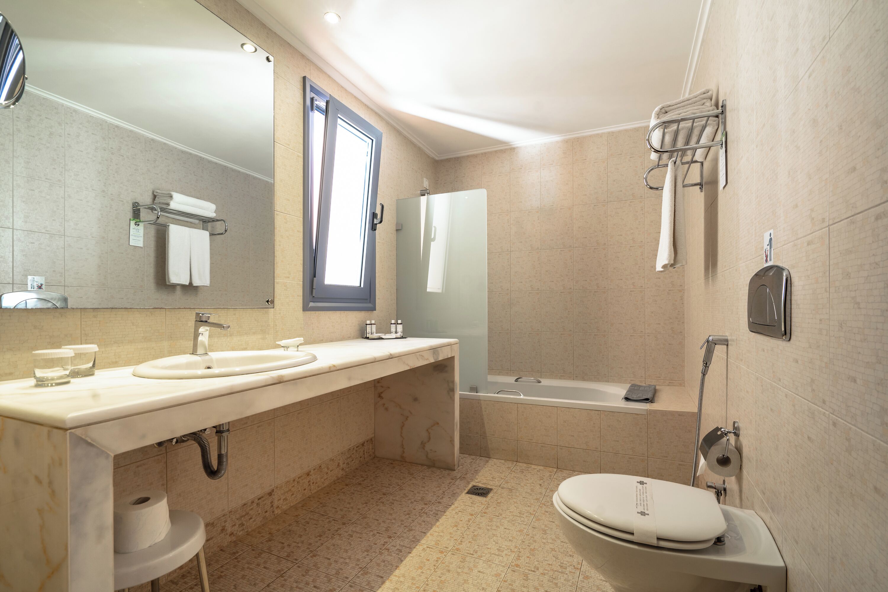 A modern bathroom with a large mirror, two sinks, a bathtub, and a toilet.