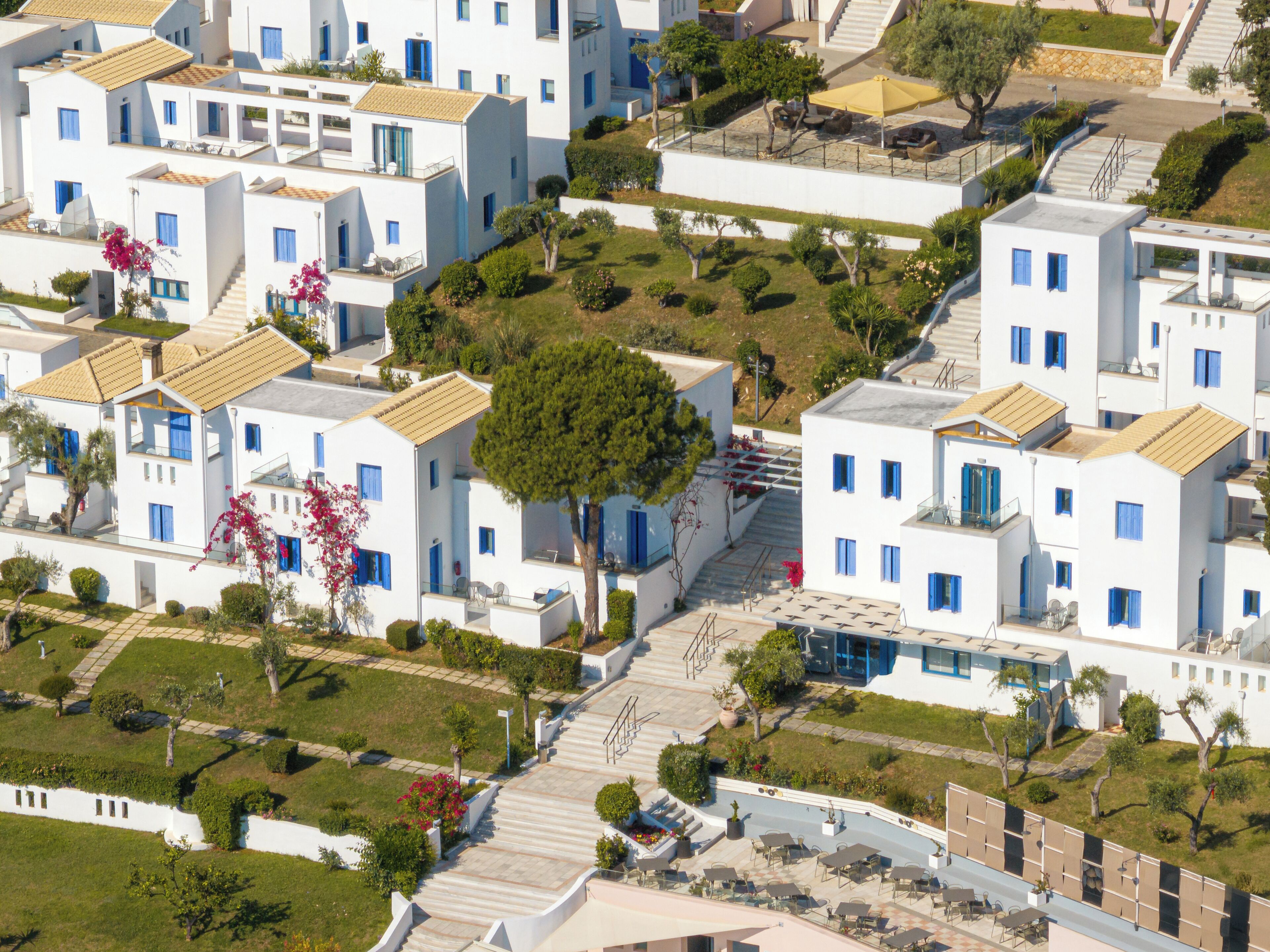 A residential area with white buildings, blue windows, and a central garden with a tree.