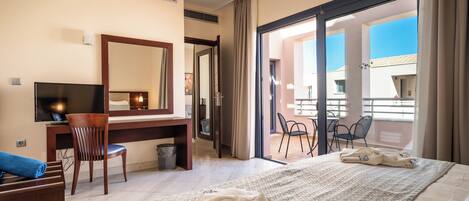 A hotel room with a bed, a desk with a chair, a television, and a balcony with chairs.