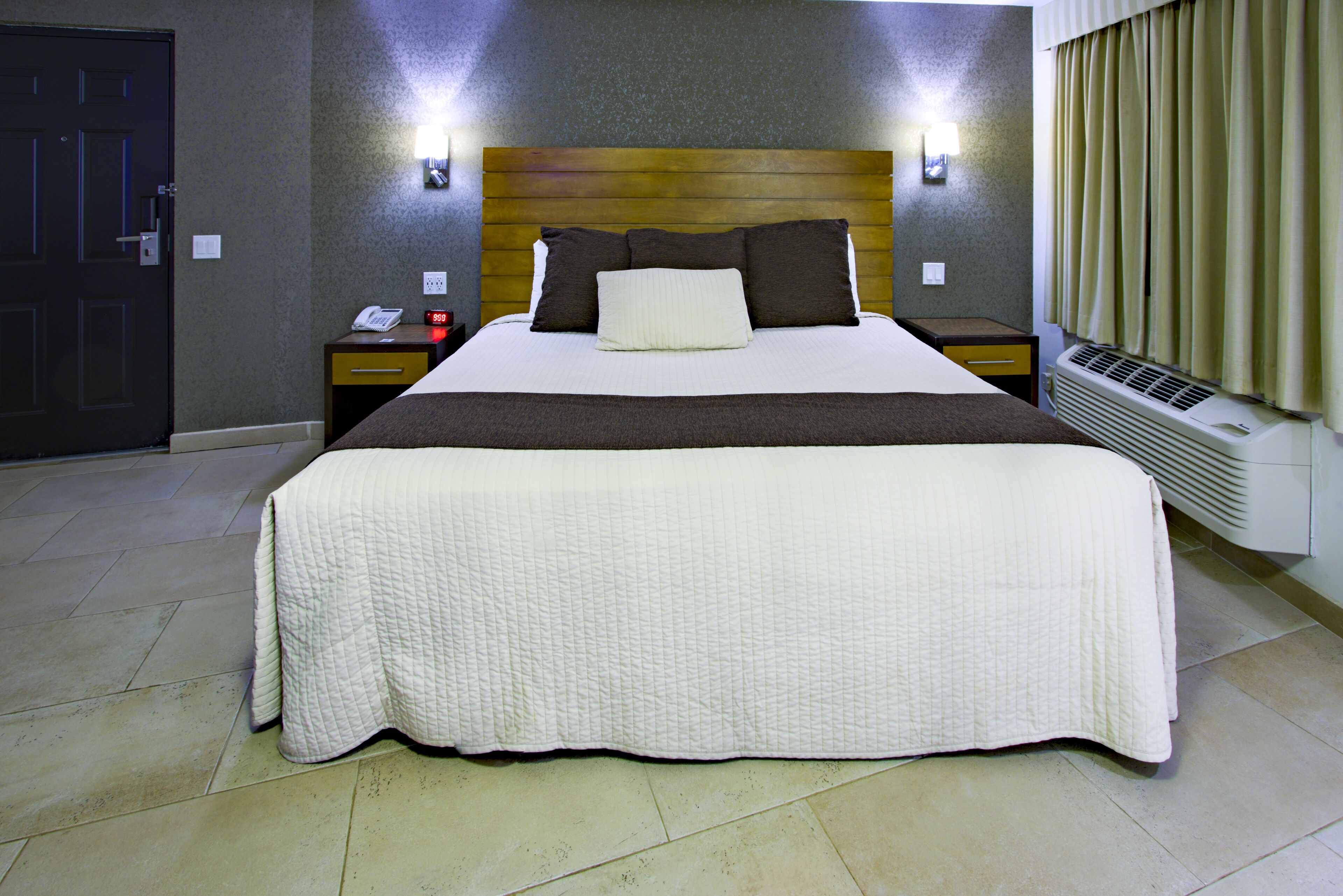 Une chambre d’hôtel avec un grand lit, une table de chevet avec un téléphone et une lampe fixée au mur.
