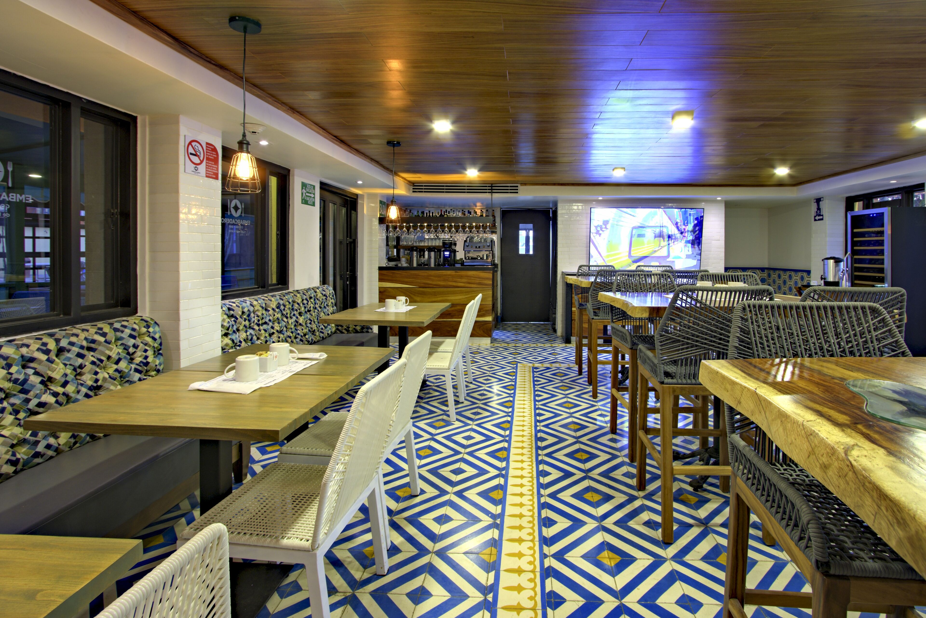A restaurant with patterned floor tiles, wooden tables and chairs, and a bar area in the background.