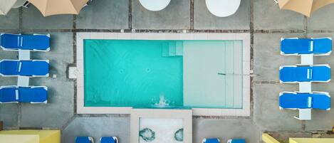 An aerial view of a pool area with multiple lounge chairs, umbrellas, and a central pool.