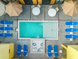 An aerial view of a pool area with multiple lounge chairs, umbrellas, and a central pool.