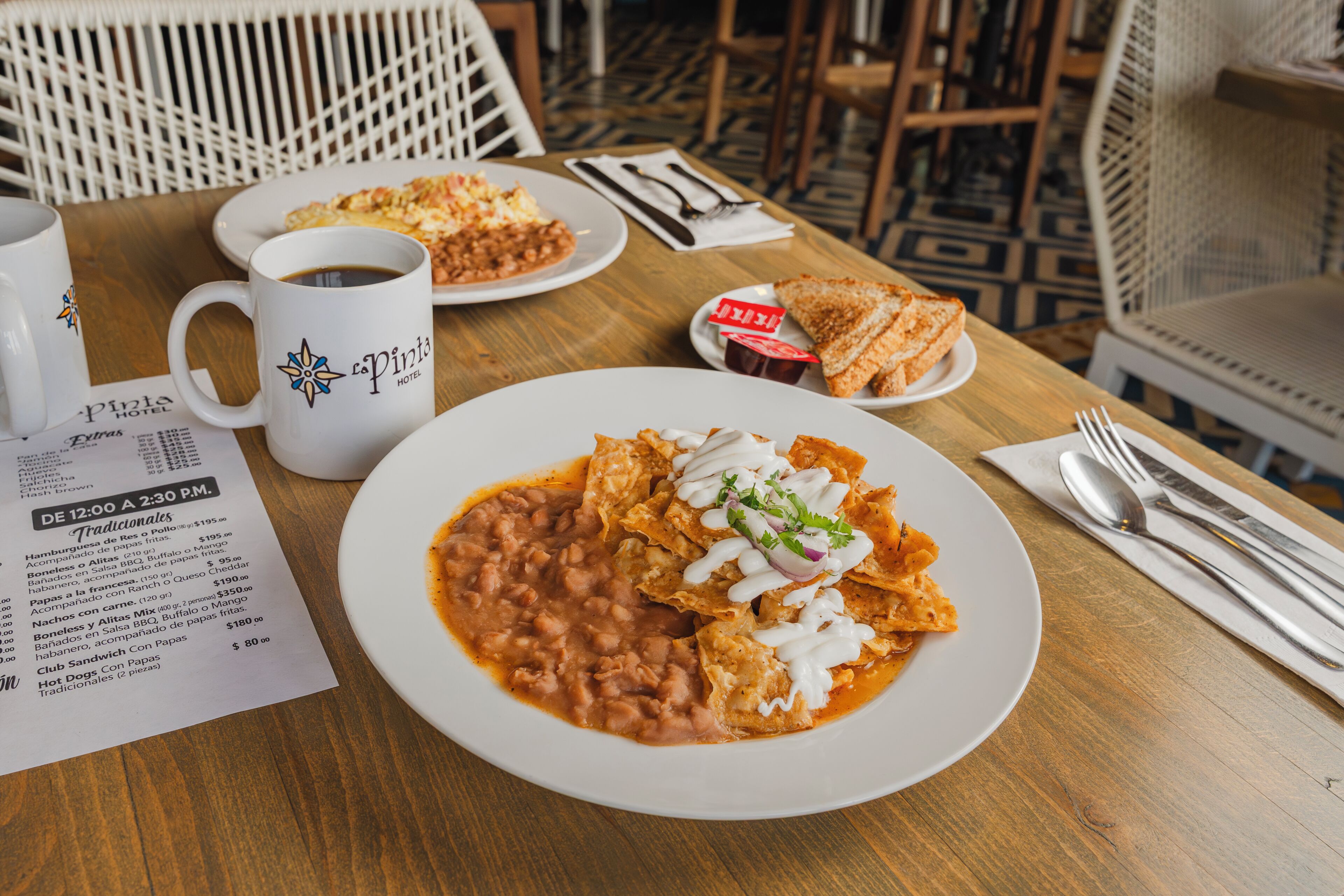 A dining table with a plate of nachos, a cup of coffee, and a menu.