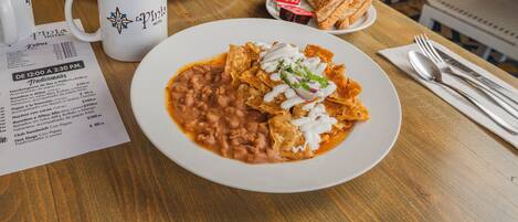 A dining table with a plate of nachos, a cup of coffee, and a menu.
