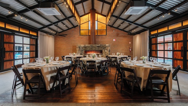 A restaurant with multiple round tables, chairs, and a brick wall with a fireplace. - Hotel La Pinta (Ensenada)