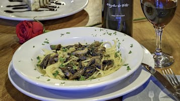 Un plato de pasta con champiñones, una copa de vino y una botella de vino sobre una mesa.