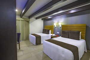 Una habitación de hotel con dos camas, una mesita de noche, una lámpara y una silla.