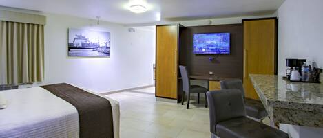 Una habitación de hotel con cama, escritorio, televisión y kitchenette.