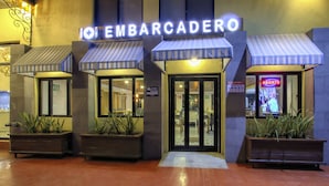 A hotel entrance with a sign reading "EMBARCADERO" and a neon "ABIERTO" sign. There are potted plants at the entrance and a tiled floor. - Hotel La Pinta (Ensenada)