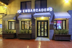 A hotel entrance with a sign reading "EMBARCADERO" and a neon "ABIERTO" sign. There are potted plants at the entrance and a tiled floor.
