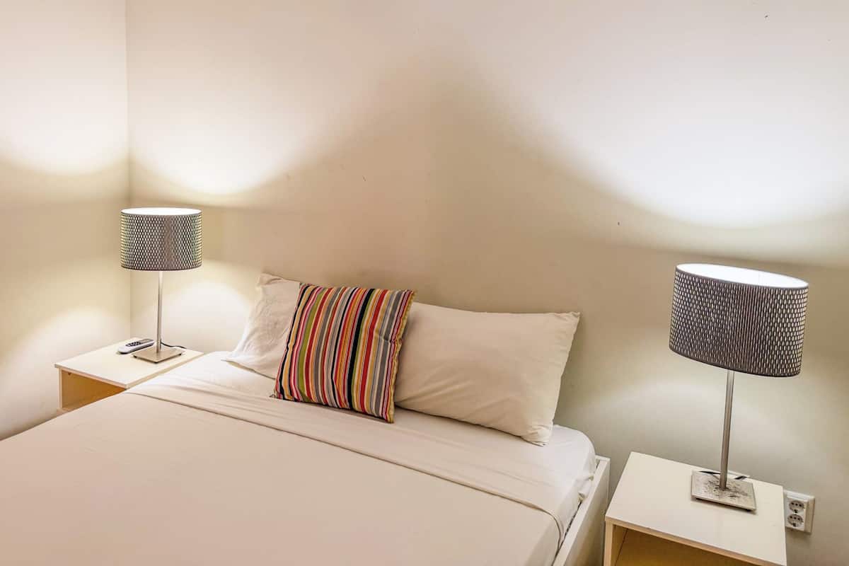 A bed with a white comforter, a striped pillow, and two bedside tables with lamps.