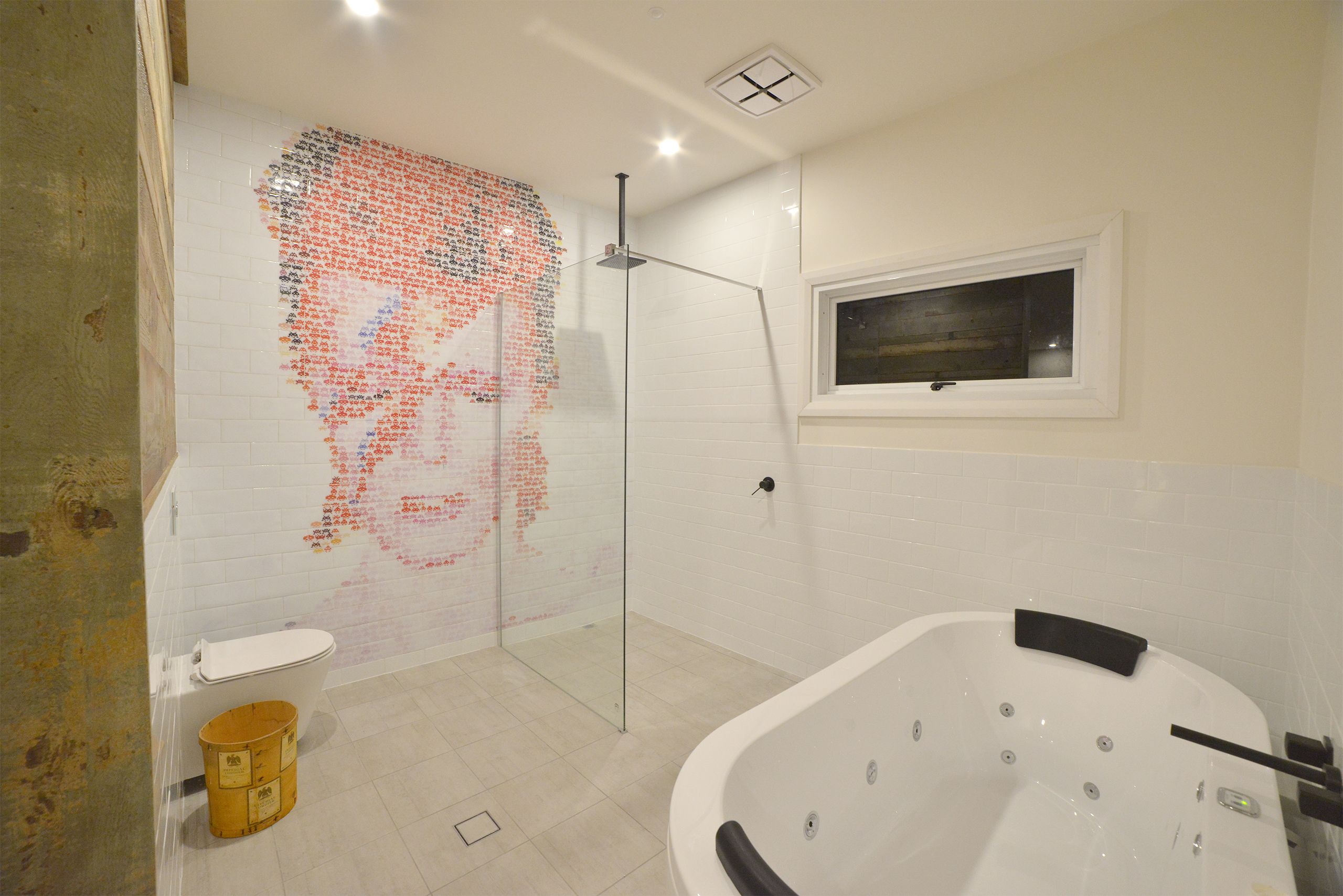 A bathroom with a glass shower enclosure, a white bathtub, and a mosaic wall art piece.