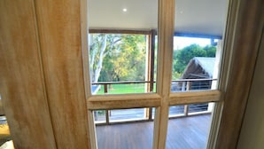 Vista desde una ventana con terraza de madera, zona exterior techada y árboles al fondo.