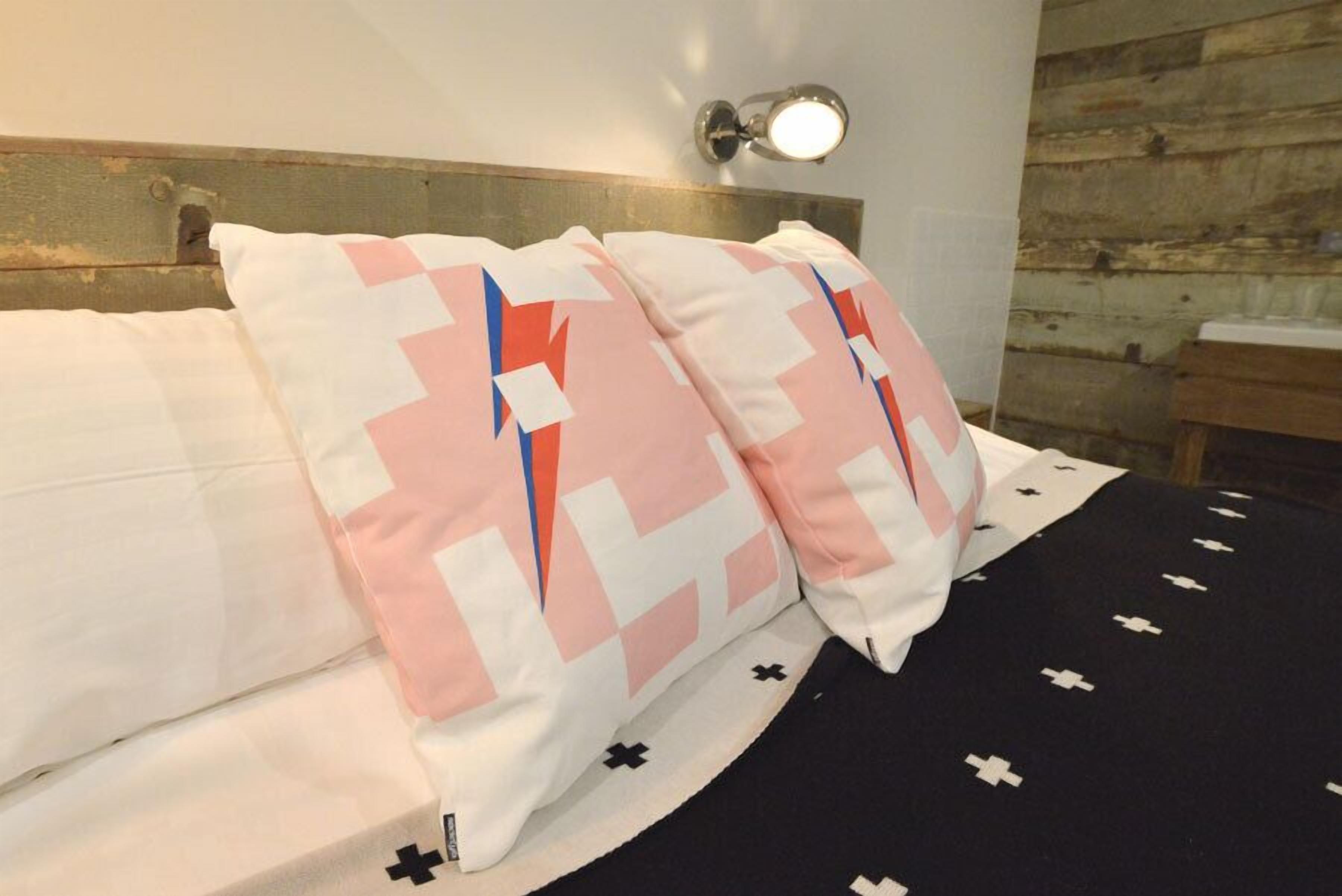 Una cama con almohadones estampados, cabecera y lámpara fijada a la pared.