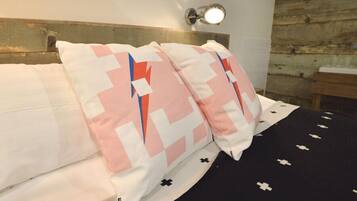 Una cama con almohadones estampados, cabecera y lámpara fijada a la pared.