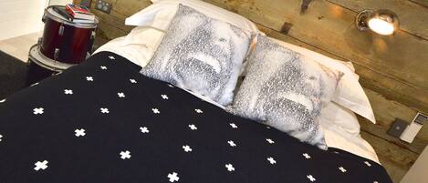 A bed with a black and white patterned bedspread, two pillows with a grey and white design, a drum set, and a wooden wall with a light fixture.