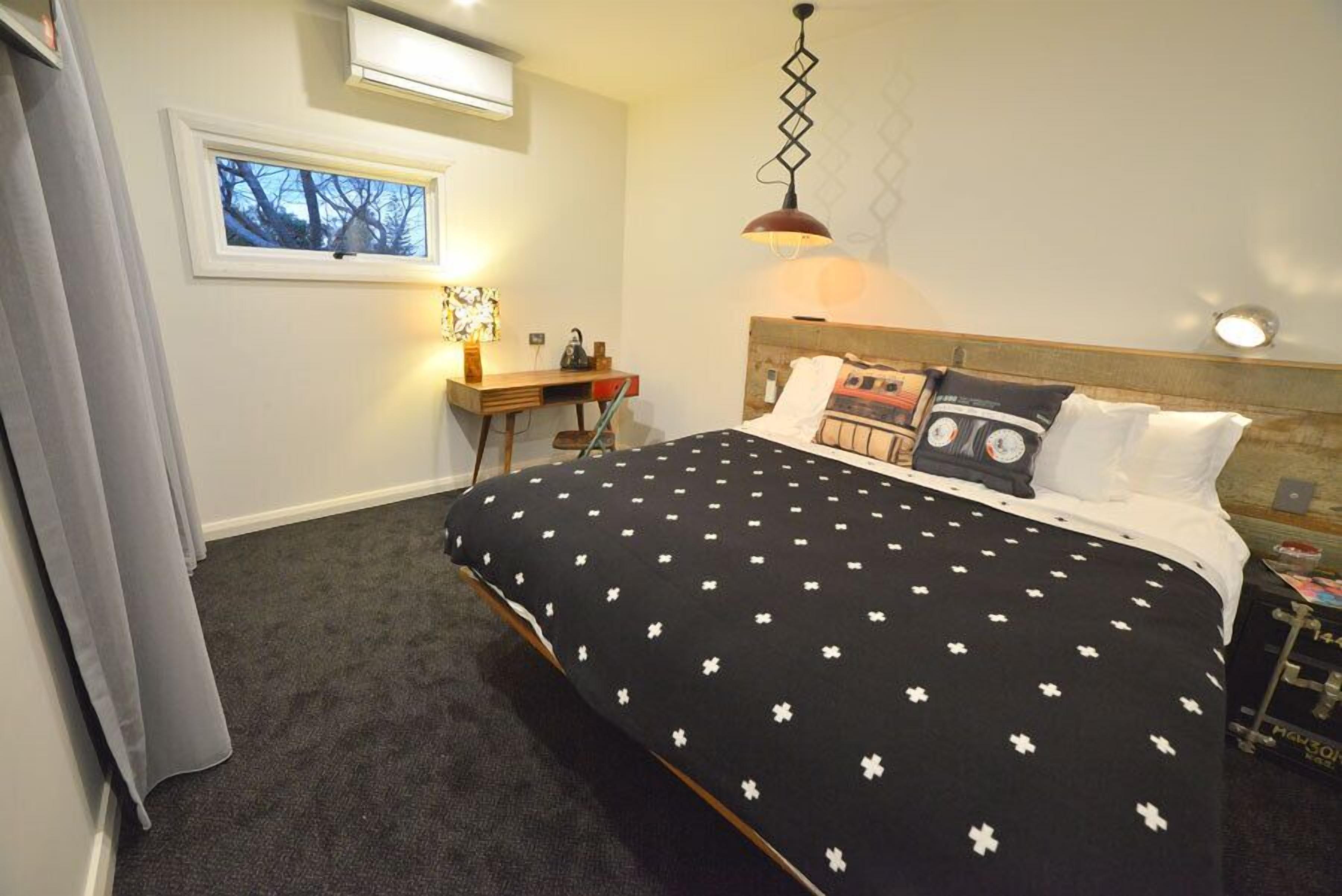 A bedroom with a large bed, a desk, a chair, a window, and a hanging light fixture.