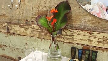 Un meuble-lavabo de salle de bain agrémenté d’un vase de fleurs, de trois verres transparents et d’un ensemble de produits de soins capillaires.