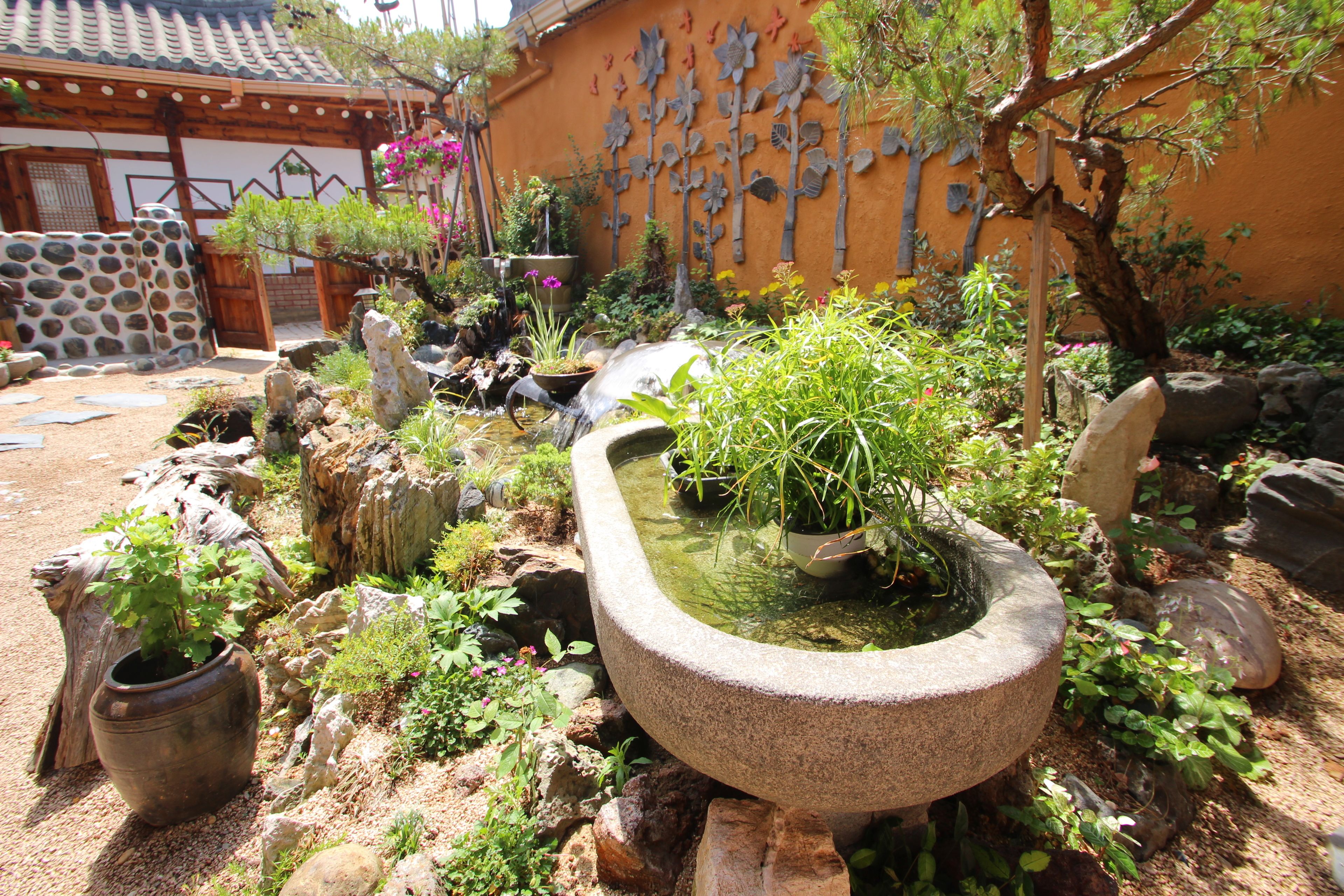 A traditional Japanese garden with a stone pond, various plants, and a wooden structure.