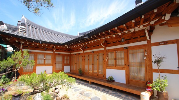 A traditional Japanese building with wooden architecture, a stone pathway, and potted plants. - Happiness Full Guesthouse (Jeonju)