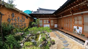 A traditional Japanese garden with a wooden building, stone pathways, and a variety of plants. - Happiness Full Guesthouse (Jeonju)