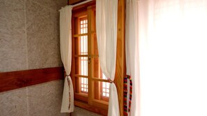A room with a wooden-framed window, white curtains tied back, and a striped item hanging on the wall. - Happiness Full Guesthouse (Jeonju)