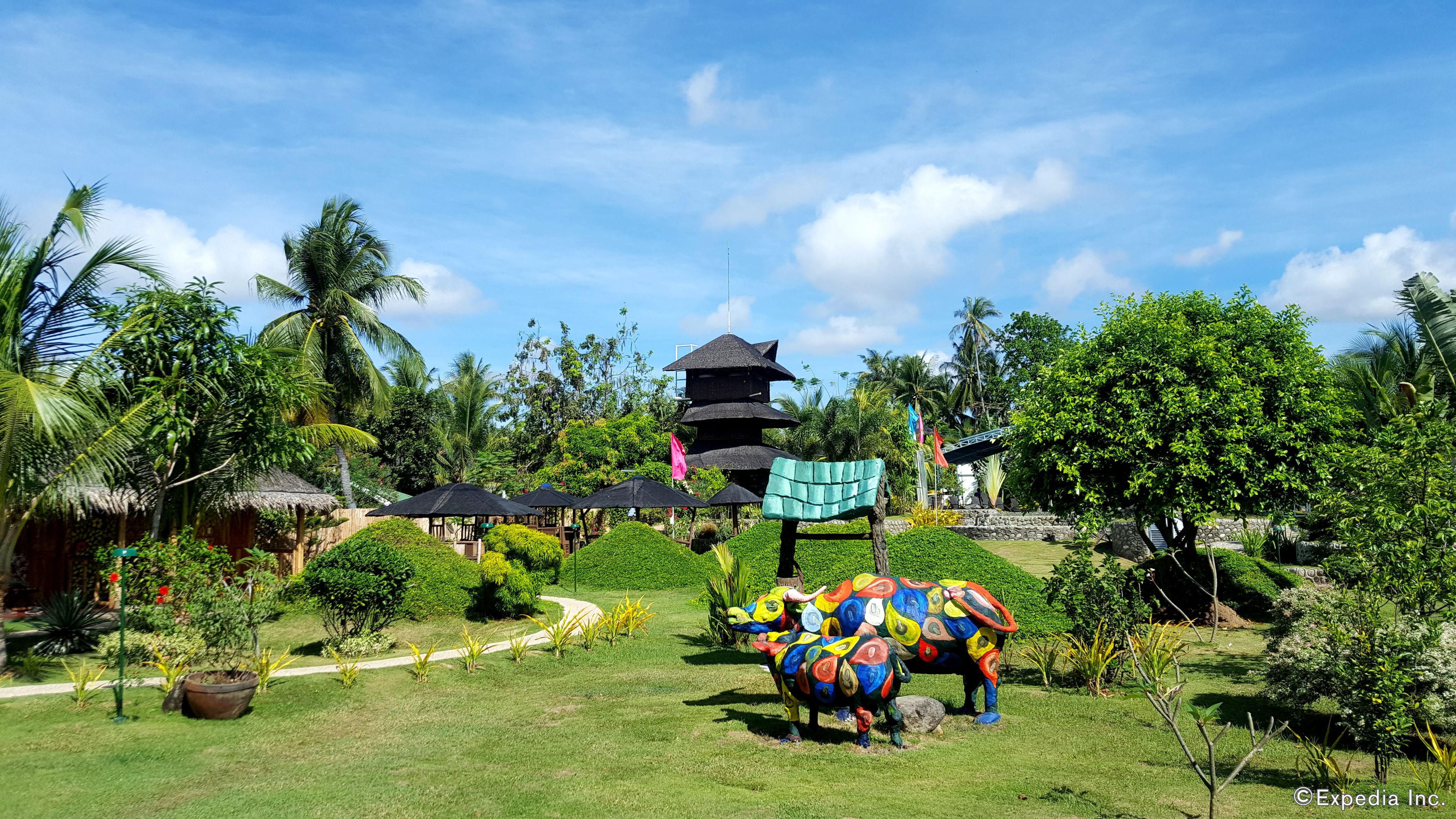 Un complexe hôtelier tropical doté d’un bâtiment à toit de chaume, d’une tour à plusieurs niveaux et d’éléphants peints aux couleurs vives.