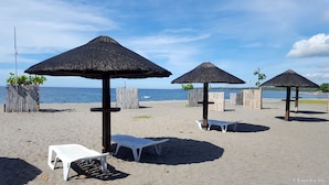 A beach with thatched umbrellas and white plastic chairs.