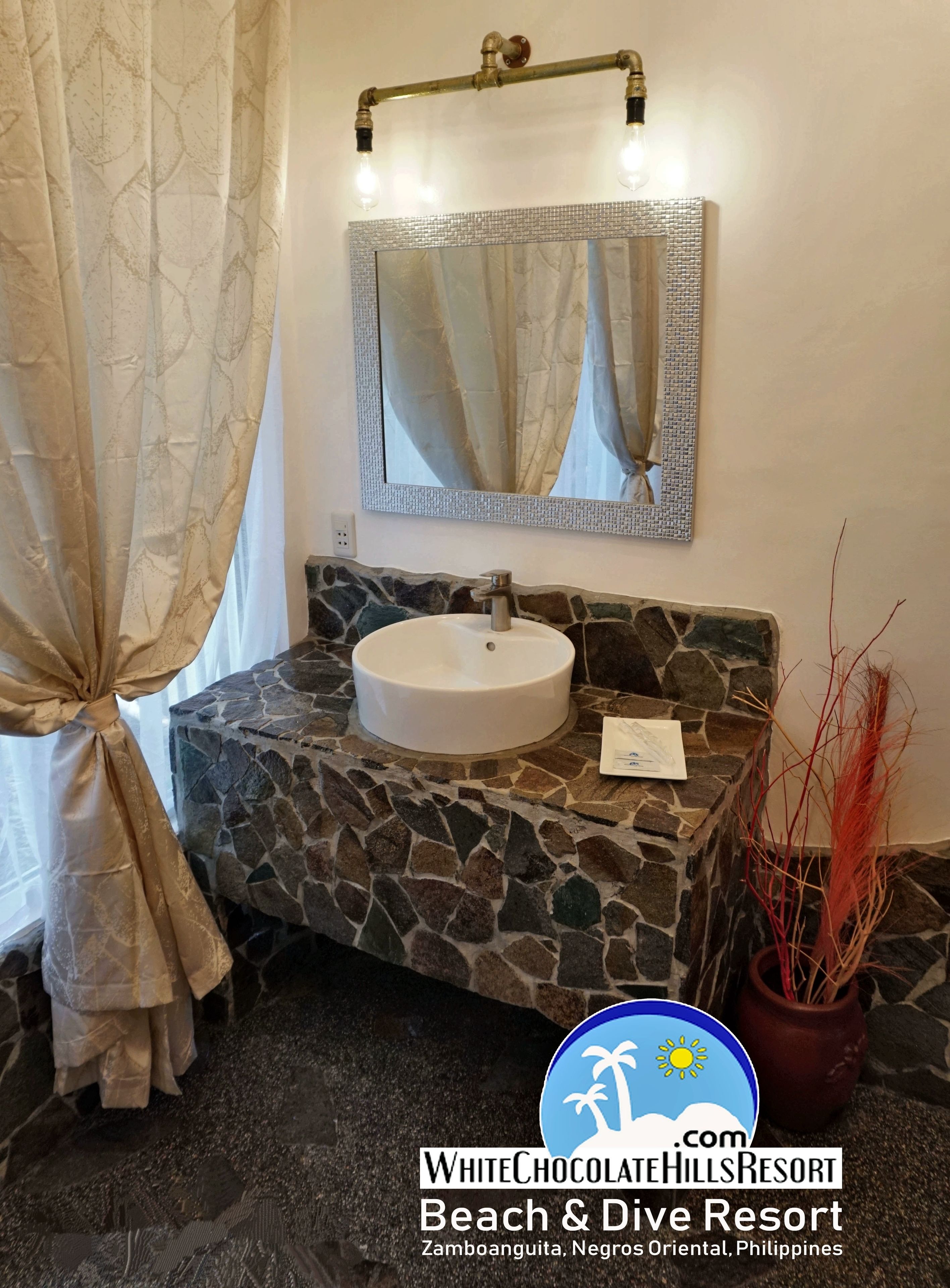 Une salle de bain avec un lavabo en pierre, un miroir doté d’un cadre texturé et une plante en pot.