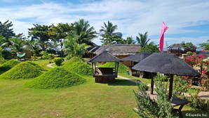 A resort with thatched-roof structures, lush green lawns, and tropical vegetation.