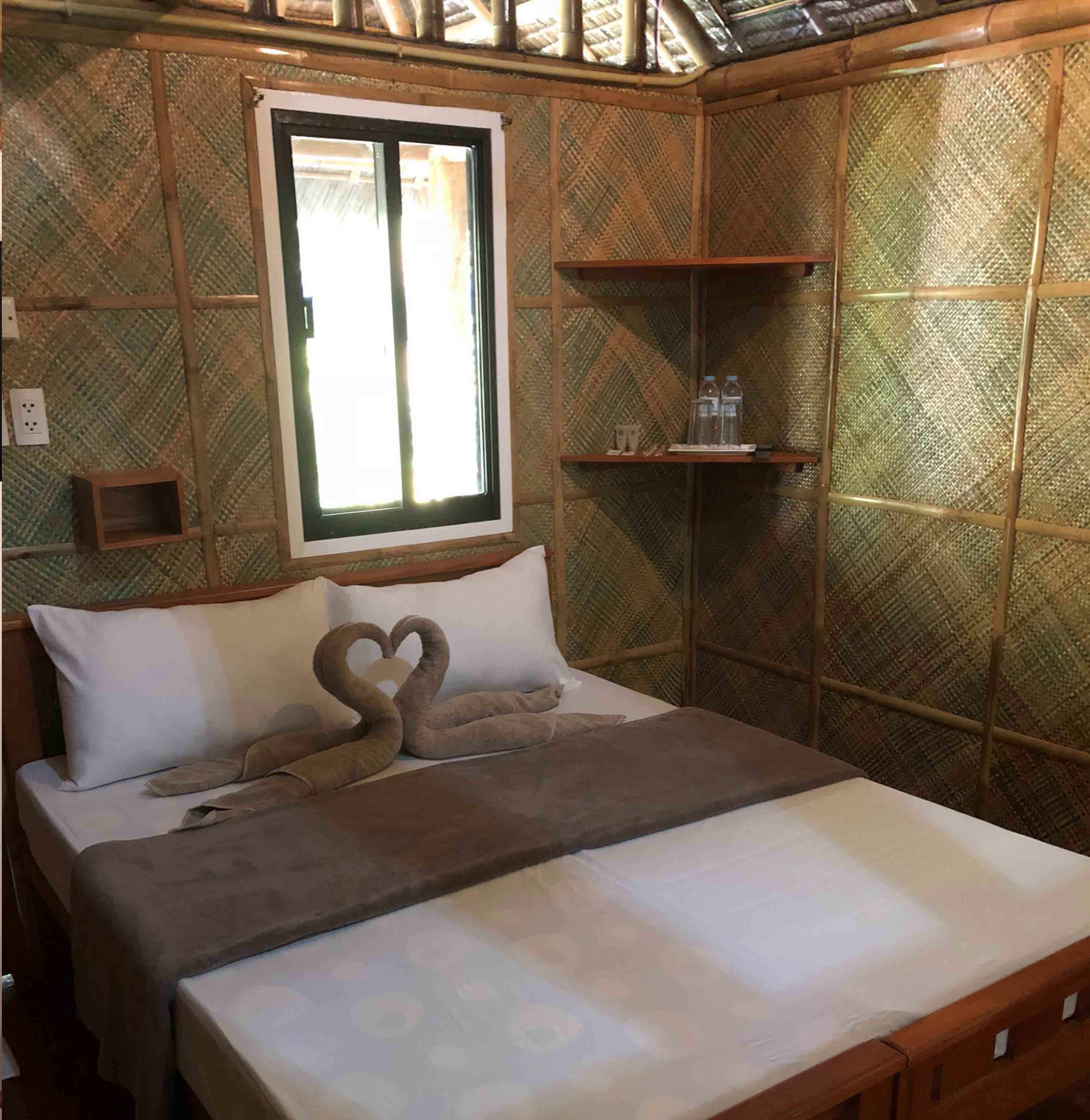 A bed with a heart-shaped pillow arrangement, a window, and a shelf with bottles.