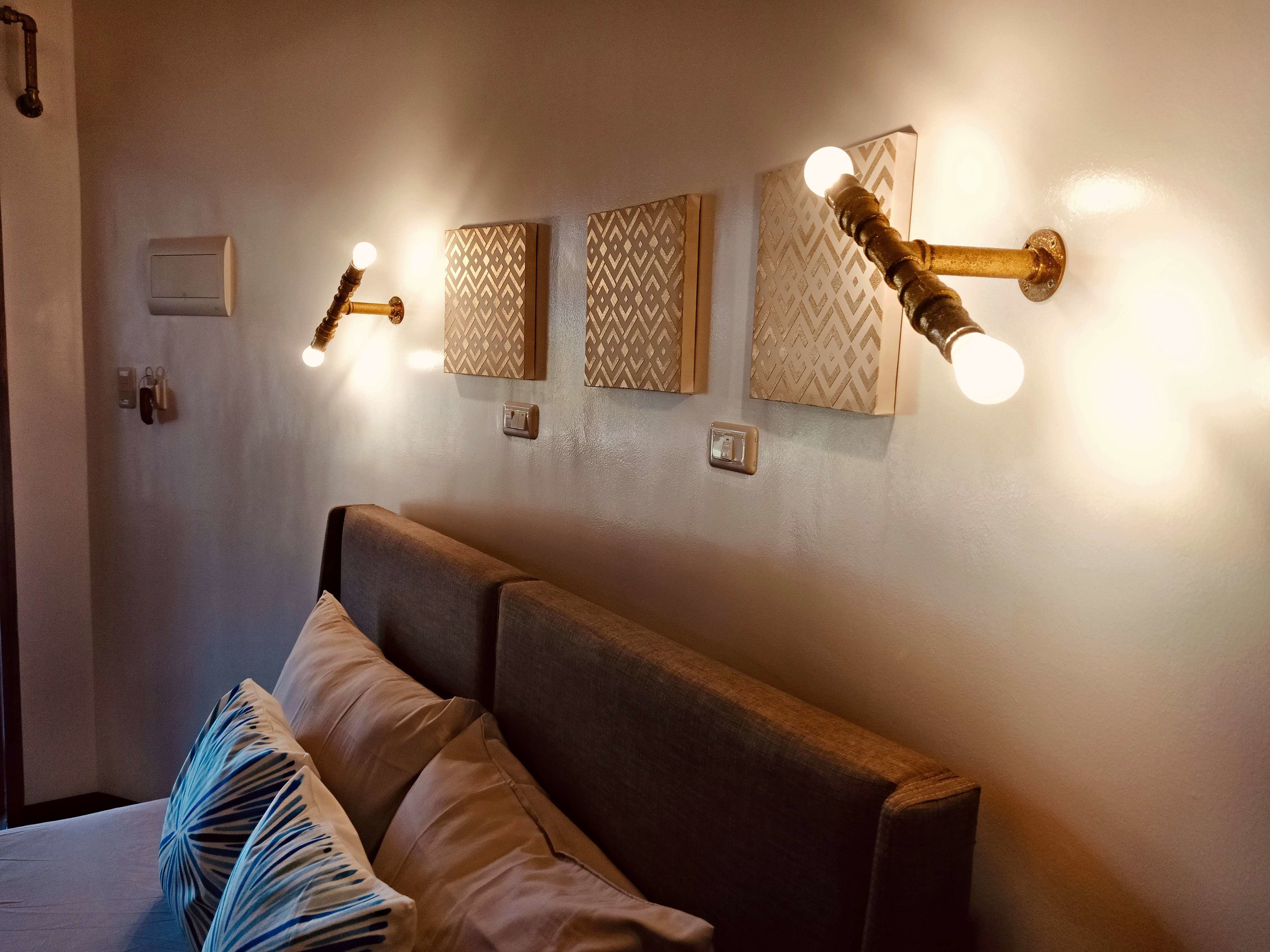 A bedroom with a bed, wall-mounted light fixtures, and a thermostat.